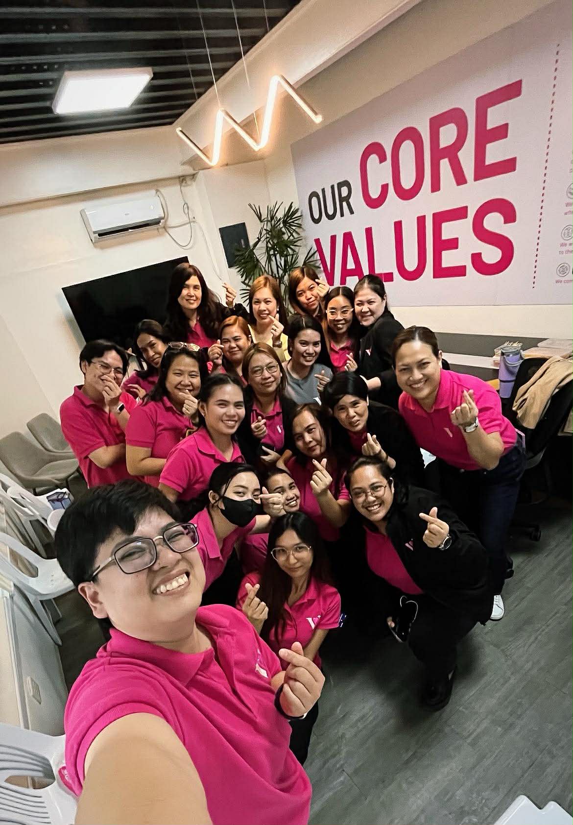 Vanity Connections team in pink uniforms in front of Our Core Values wall